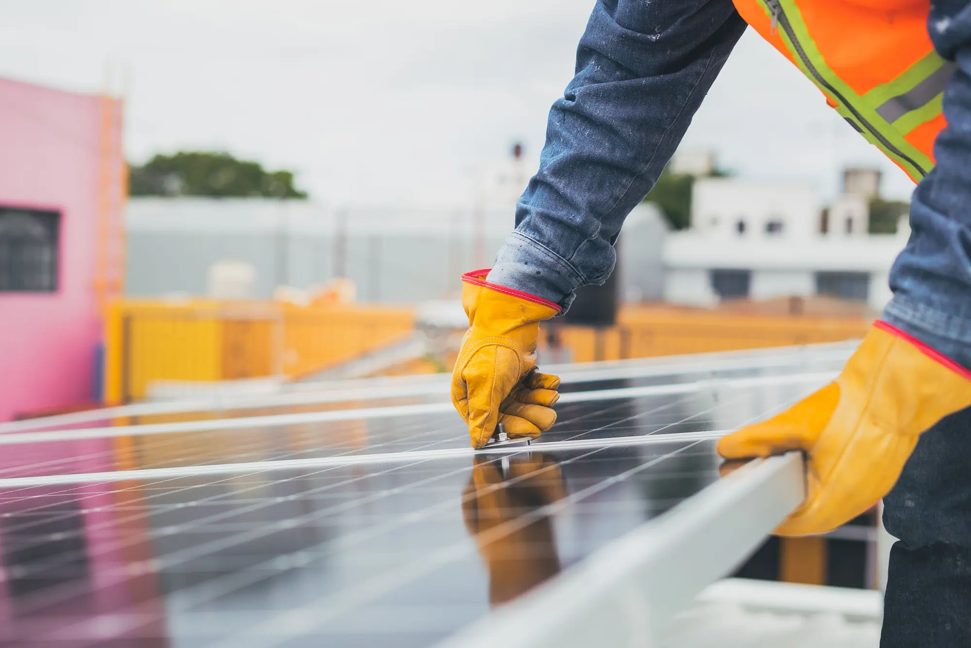 An installer in gloves and a safety vest seating a solar panel on its frame