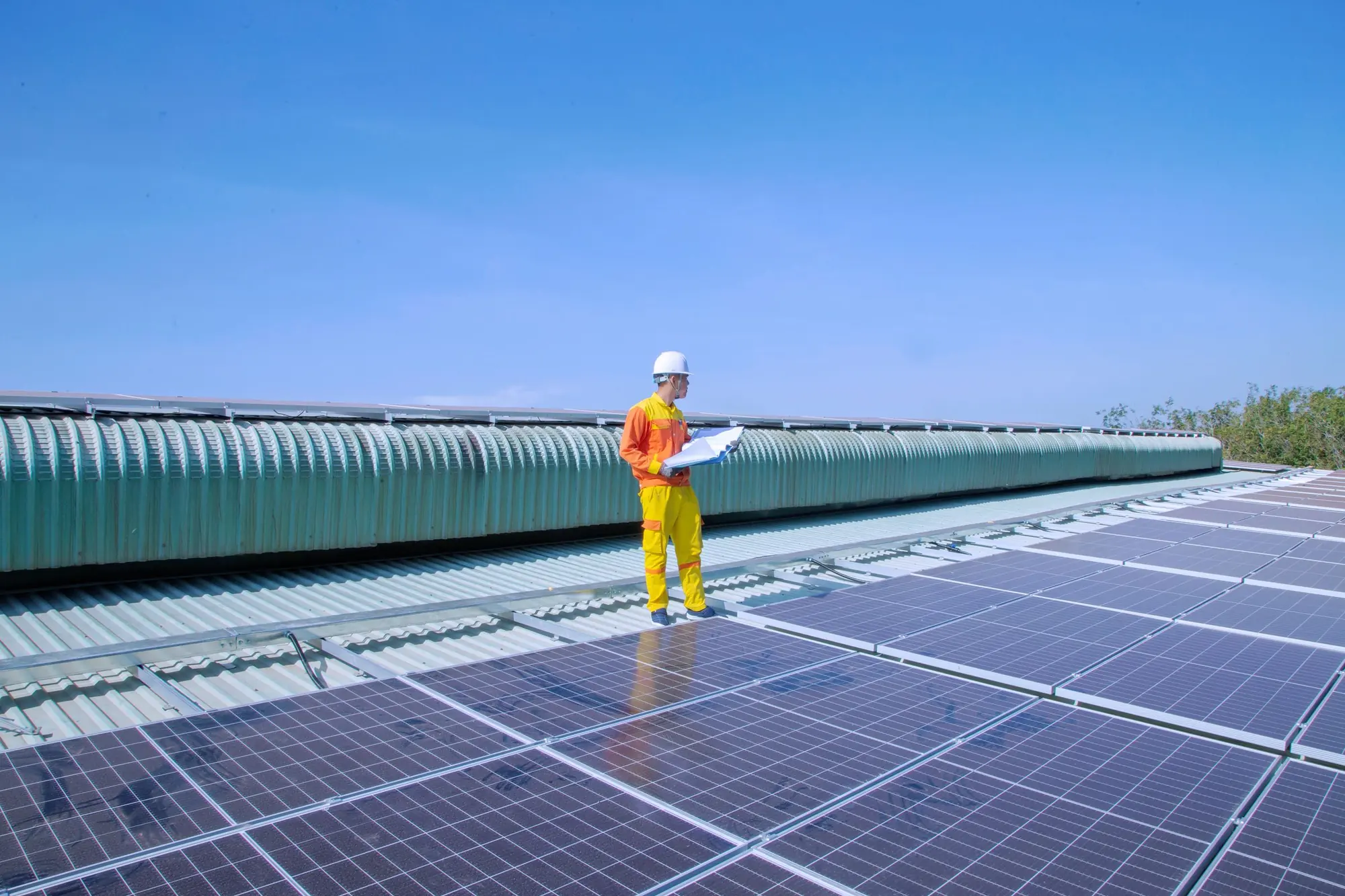 An engineer in a hard hat checking a plan on a rooftop solar array